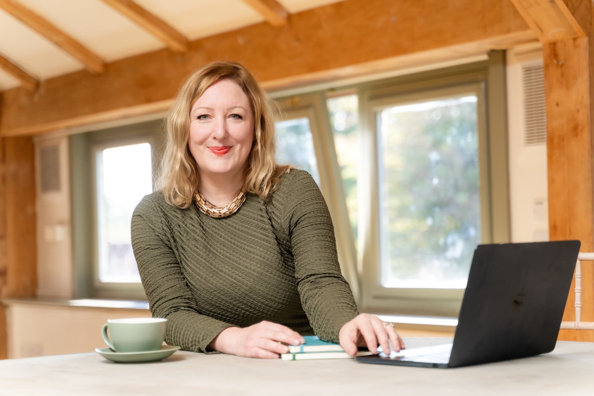 Laura Garwood working at a table with a laptop and a cup of coffee in a warm, timber-lined room